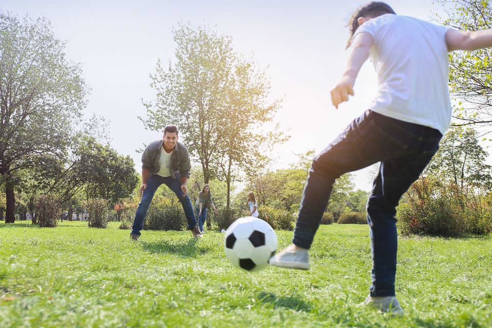 Een vader en kinderen voetballen samen in het park