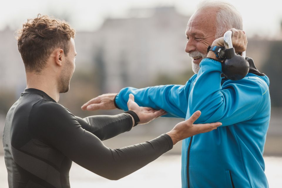 Een trainer helpt een oudere man bij een rekoefening
