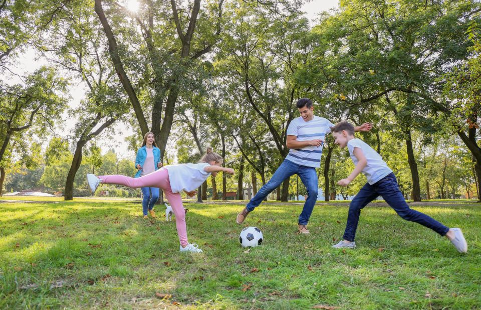Een opa voetbalt met zijn kleinkinderen op het gras in het park